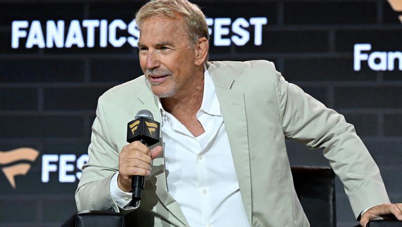 Kevin Costner îmbrăcat cu un costum bej, vorbin la o emisiune