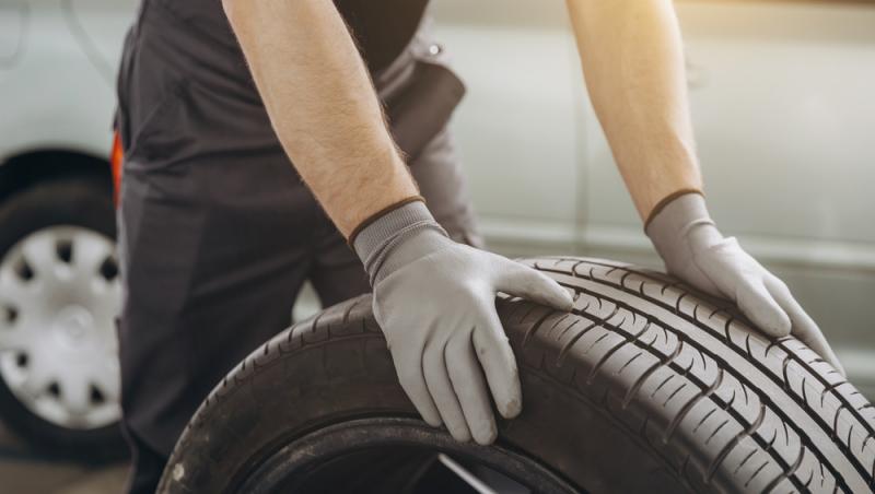 imagine cu un mecanic auto ținând un pneu în atelierul de reparații. Înlocuirea pneurilor de iarnă și de vară
