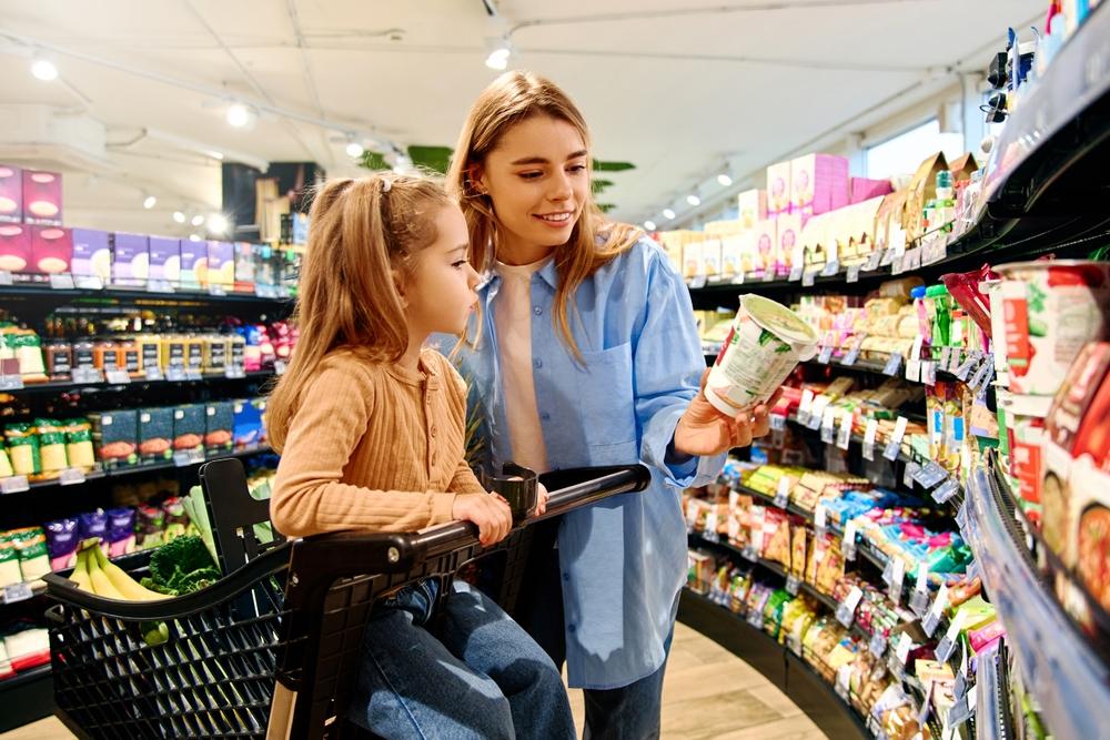 mamă care îi citește ingredintele de pe un produs copilei sale în supermarket