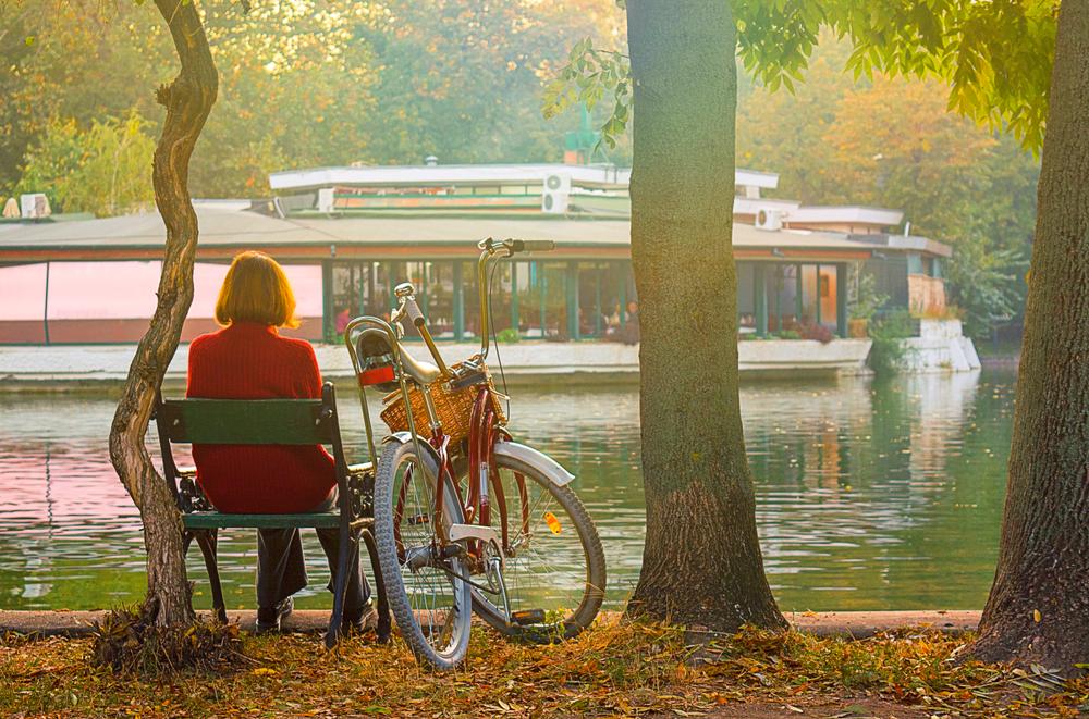 femeie care privește de pe bancă un vaporaș pe lac în parc. lângă ea este o bicicletă