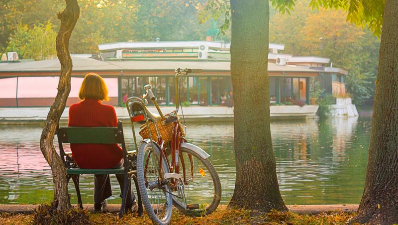 femeie care privește de pe bancă un vaporaș pe lac &icirc;n parc. l&acirc;ngă ea este o bicicletă