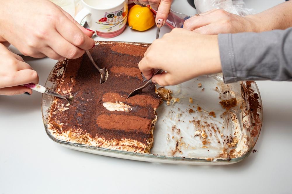 mâini care iau cu lingura dintr-o tavă de tiramisu