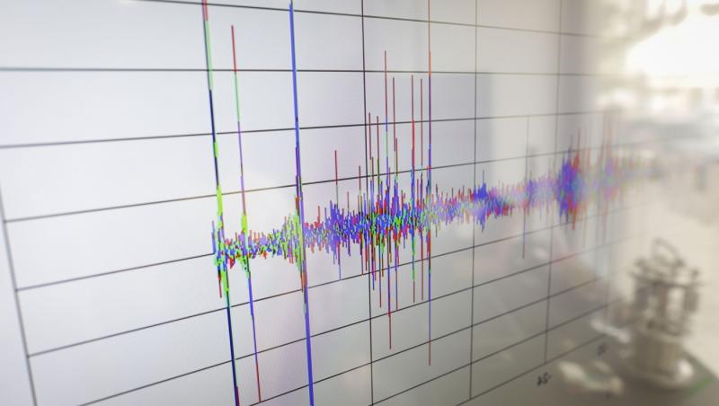 Detalii cu profunzime mică a c&acirc;mpului (focalizare selectivă), surprinz&acirc;nd oscilații pe o seismogramă afișată pe un ecran digital, cu reflexia unui dispozitiv vizibilă &icirc;n partea dreaptă.