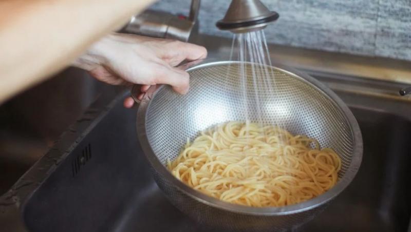 m&acirc;ini care țin strecurătoarea cu paste sub jetul de apă de la chiuvetă