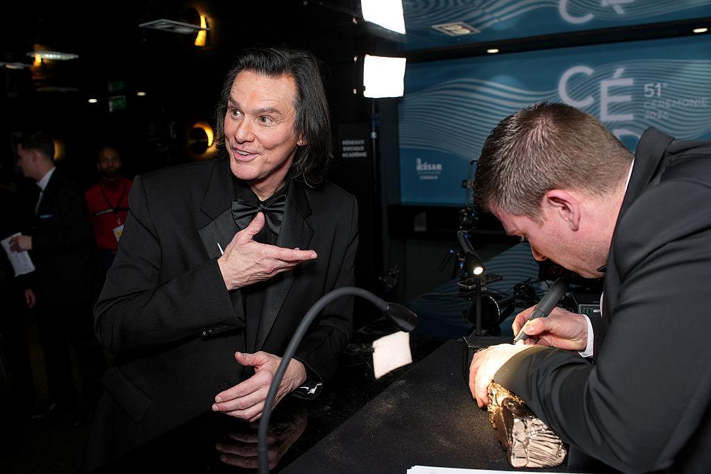 Jim Carrey ține în mână un premiu și poartă un costum închis la culoare