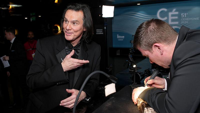 Jim Carrey ține &icirc;n m&acirc;nă un premiu și poartă un costum &icirc;nchis la culoare