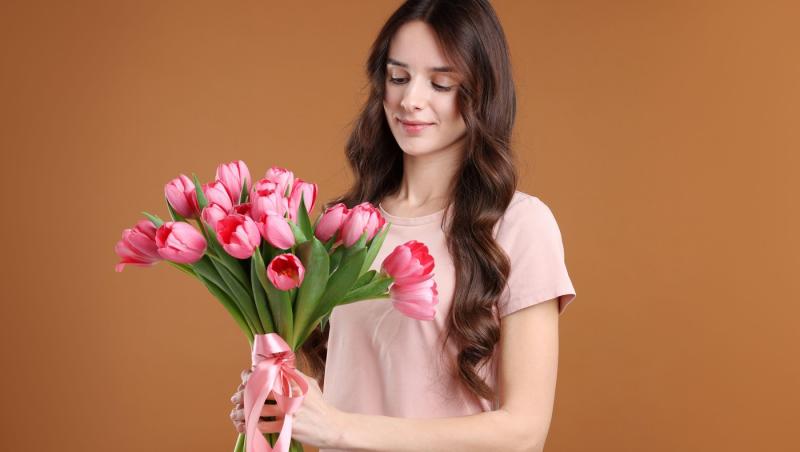 fată frumoasă care ține &icirc;n m&acirc;nă un buchet de flori