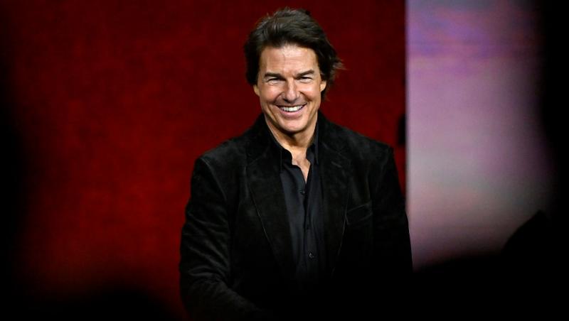 Tom Cruise poartă o bluză neagră pe un fundal &icirc;nchis la culoare