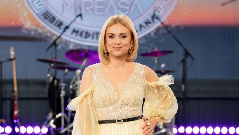 Simona Gherghe poartă o rochie deschisă la culoare pe un fundal deschis la culoare