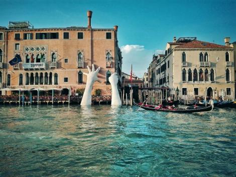 Degradarea și schimbările climatice pot ”închide” cel mai vizitat oraș din Europa! Două mâini uriaşe de copil sprijină o clădire din Veneția