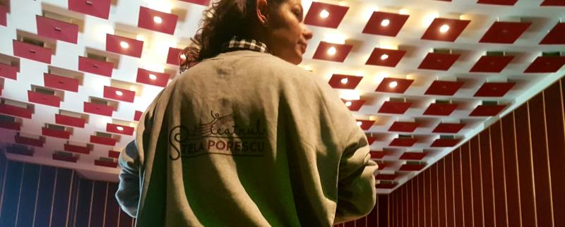 Ioana Macarie cu spatele, purtând o jachetă pe care scrie Teatrul „Stela Popescu”
