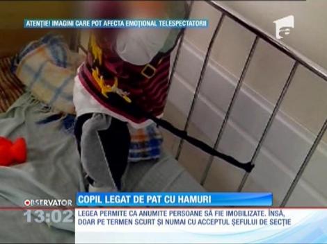 Copil legat de pat cu hamuri