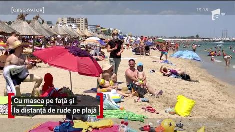 Cu masca pe față și la distanță de rude pe plajă